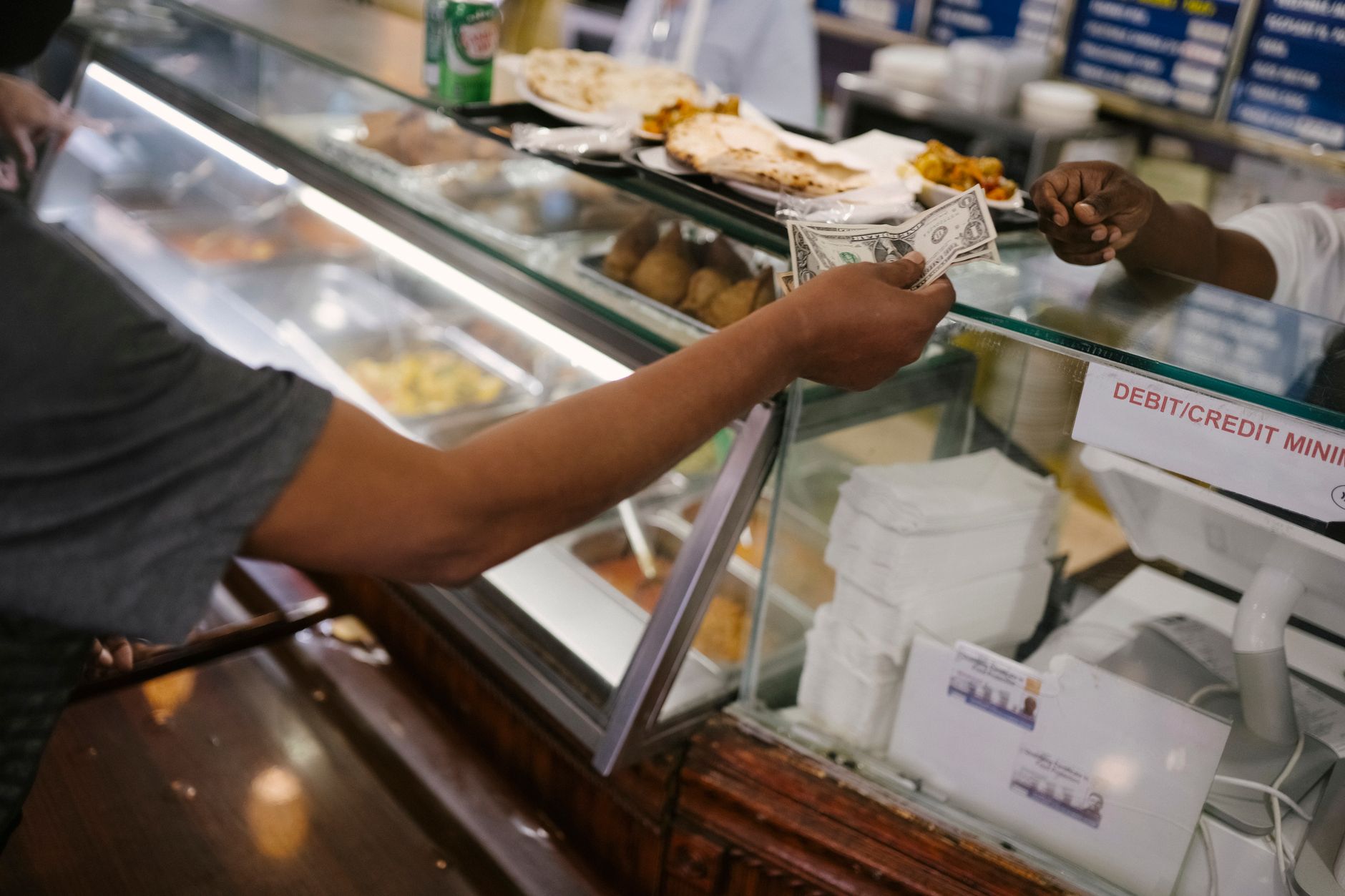 Person passing cash payment at a cafe checkout counter. Photo by Tim Samuel on Pexels