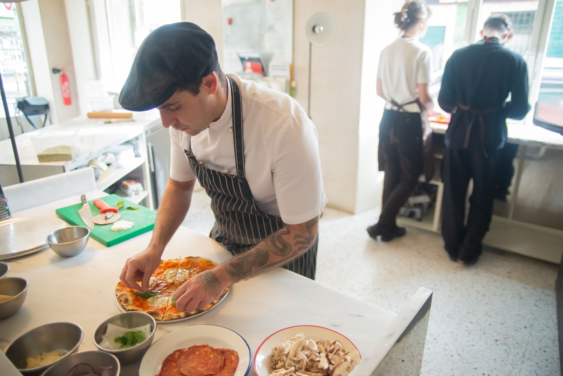 Chef preparing pizza in a professional kitchen setting, adding fresh ingredients to the dish. Photo by Kampus Production on Pexels
