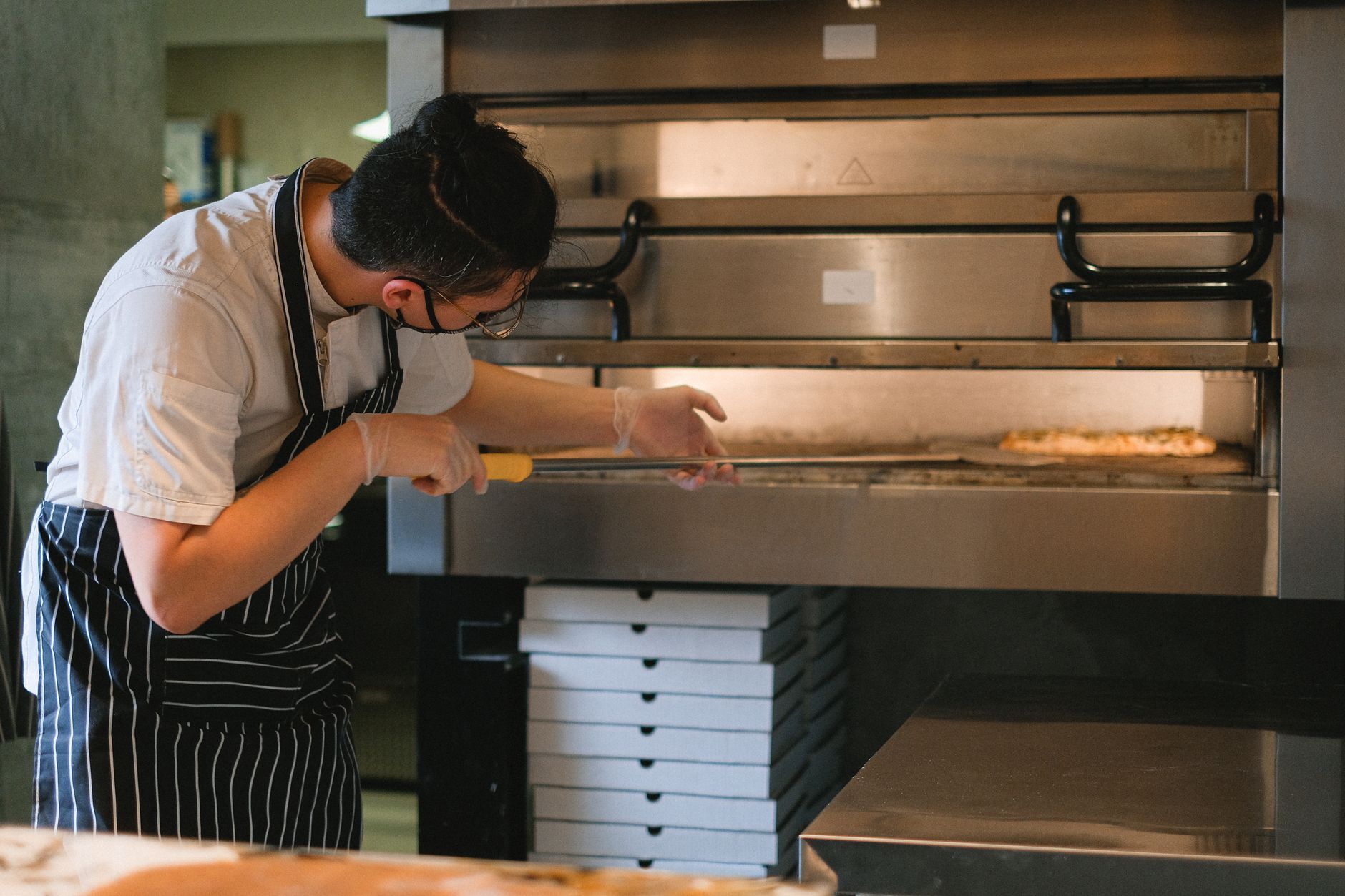 A chef in an apron prepares pizza in a commercial kitchen oven. Photo by Anna Shvets on Pexels
