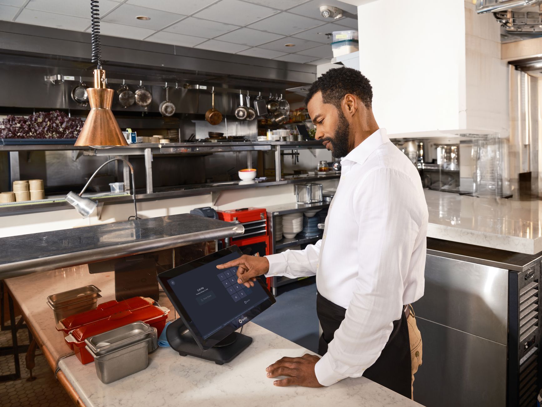A restaurant worker operates a point of sale system in a commercial kitchen setting. Photo by SpotOn POS on Pexels