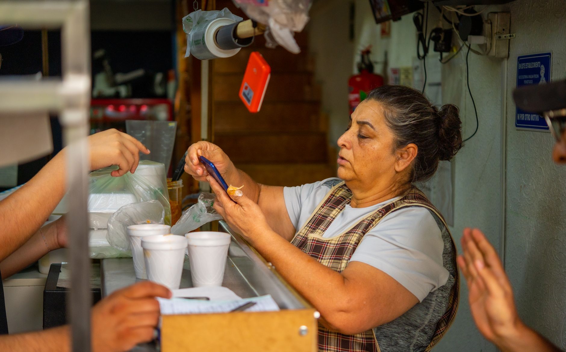 Busy food stall scene with woman serving customers, holding smartphone. Photo by Israel Torres on Pexels