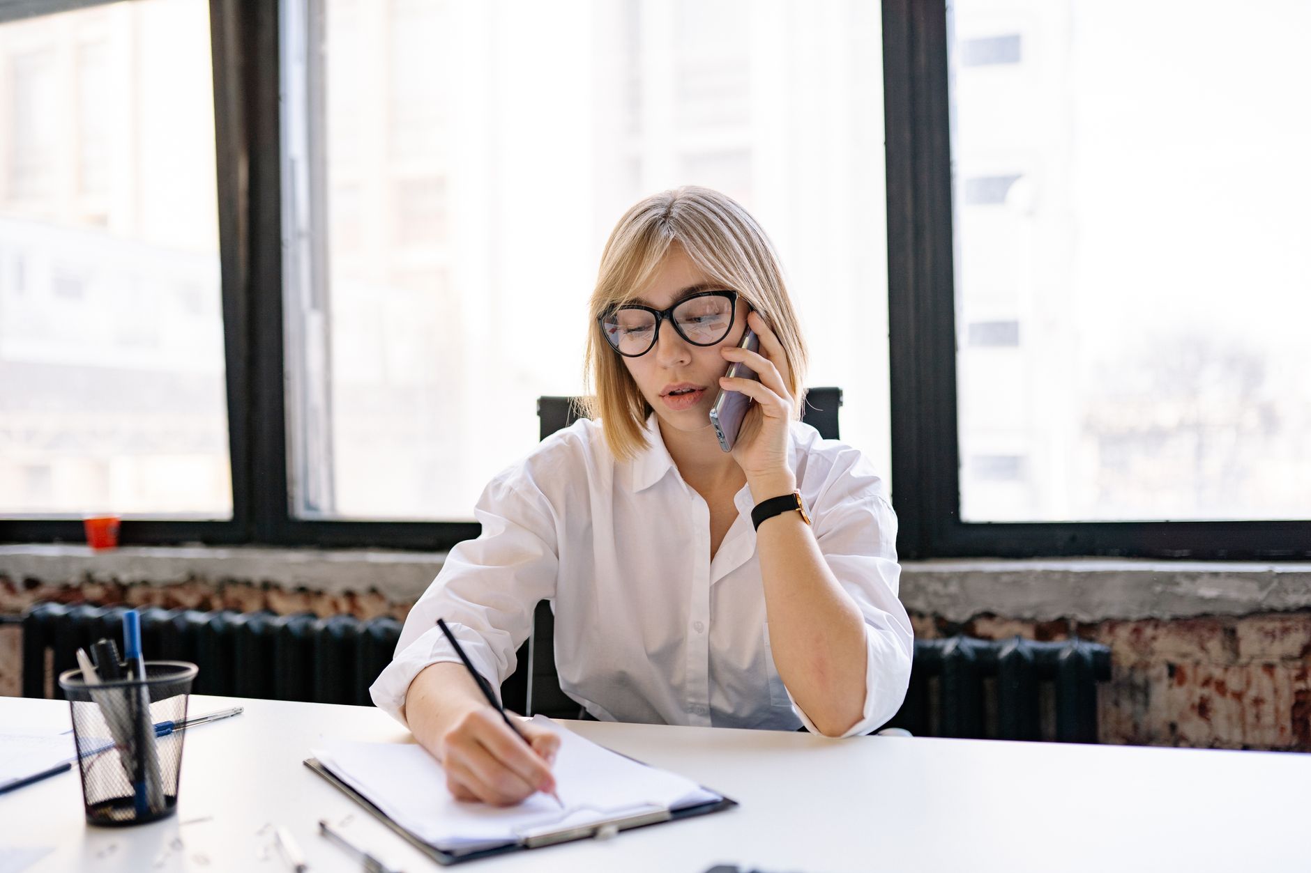 A woman in an office setting multitasking with a phone call and taking notes. Photo by Yan Krukau on Pexels