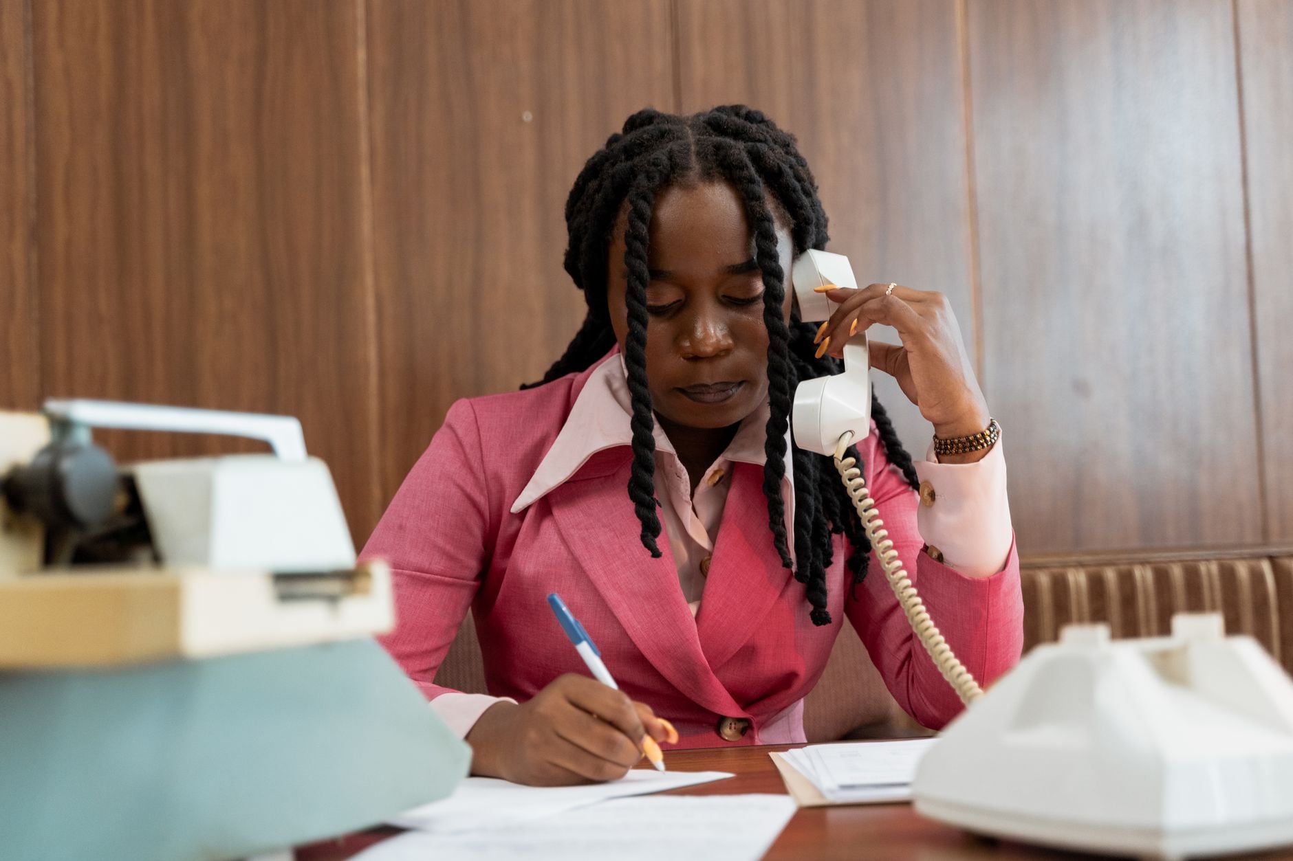 Professional woman in 80s style business attire making notes during a phone call. Photo by MART  PRODUCTION on Pexels