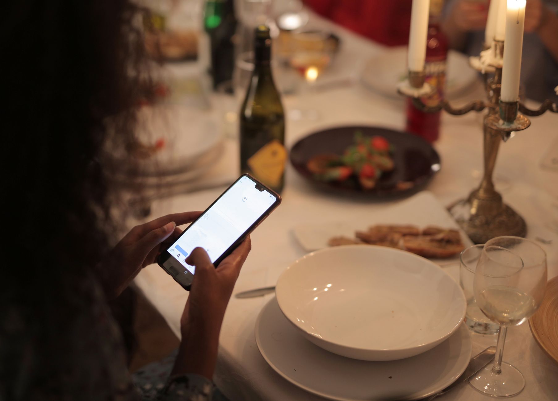 Woman using smartphone at candlelit restaurant table. Photo by Andrea Piacquadio on Pexels